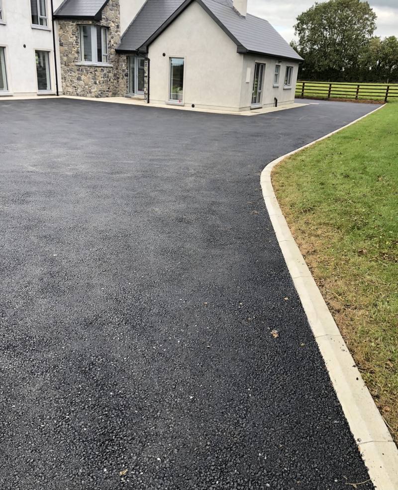 A tarmac driveway with a long kerbed edge along the lawn