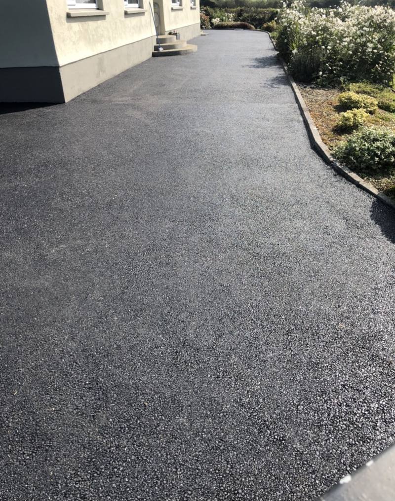 A tarmac path along a house, beside the shrubs