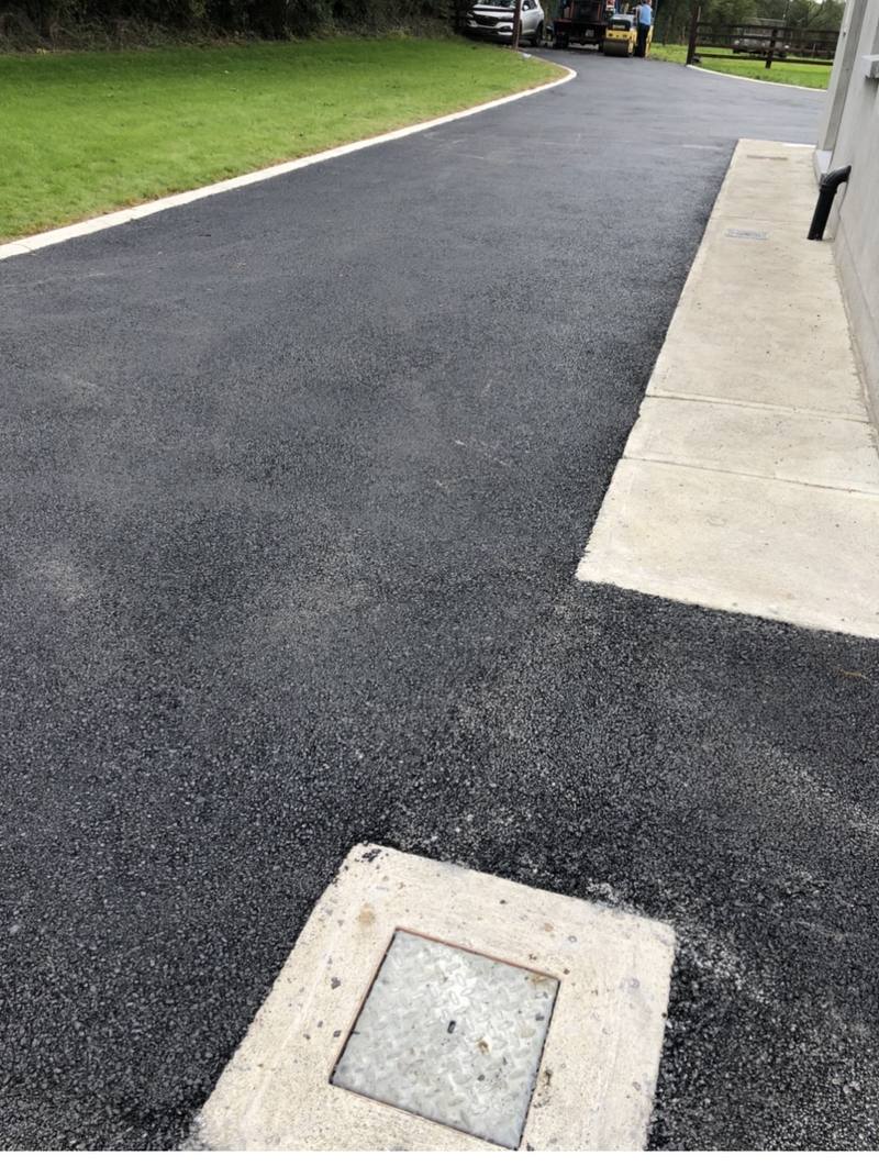 A tarmac driveway along the side of a house, laid neatly round a service cover