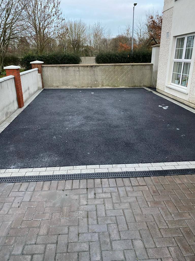 A small tarmac driveway with a channel drain where it meets the paving